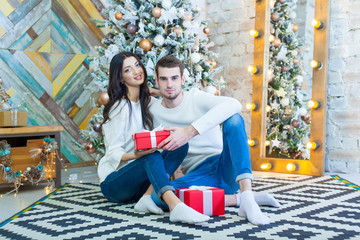 Obraz na płótnie Canvas Young beautiful couple sitting near Christmas tree with xmas giftsin red boxe.