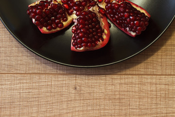 Ripe Azerbaijani pomegranate on a black plate and on a wooden table