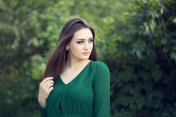 Portrait of an young attractive woman with long brown hair enjoying her time in the park with green tree in background.