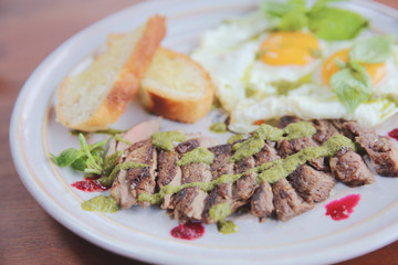 Grilled beef steak with toast , fried egg and vegetables on top with pesto sauce