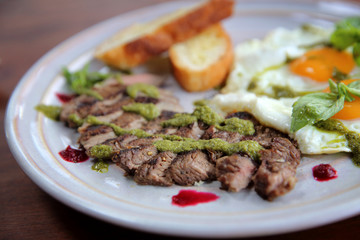 Grilled beef steak with toast , fried egg and vegetables on top with pesto sauce