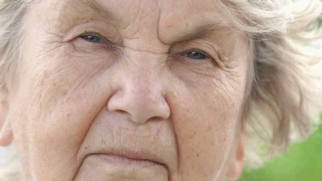 Portrait of serious mature old woman with gray hair outdoors at the street in summer. Close-up