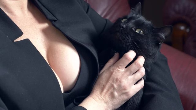 A hot woman with a big breast sits in an armchair and caresses a black cat. 4k, slow motion
