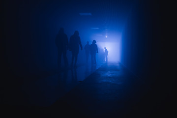 Fototapeta na wymiar silhouette of people walking in a tunnel in smoke against a background of bright light
