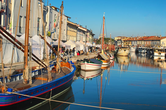 CESENATICO, ITALY: 01 JANUARY 2017- Christmas Fair kiosks on the embankment of the port channel with the typical fishing boats of the Adriatic Sea
