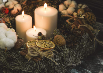 Three white candles, pinecones and twigs in a christmas wreath on a dark background