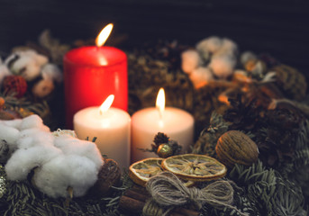 One red and two white candles in a wreath with natural christmas decorations