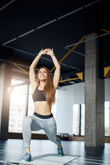 Obraz premium Beautiful female fitness idol making squats smiling early in the morning in empty gym. Portrait of fit woman training hard.