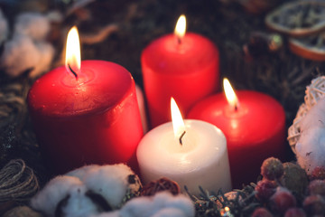 Four burning christmas candles in a wreath with natural decorations closeup