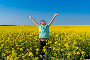 Naklejka na ściany i meble Positive young boy jumping in yellow rapeseed field. Happiness, sunshine, yellow flowers and blue sky