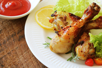 Grilled chicken legs with mustard on wooden table served on white plate with rosemary. BBQ dinner background