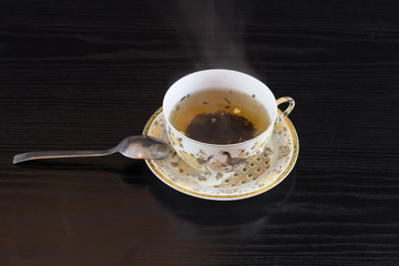  White cup in golden brown hot tea patterns and a saucer-based spoon isolated on black background 