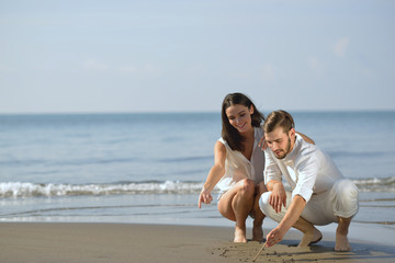 Fototapeta na wymiar Romantic young couple draw heart shapes in the sand while on honeymoon. summer beach love concept.