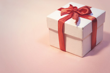 white  gift box with thin red ribbon on pink background