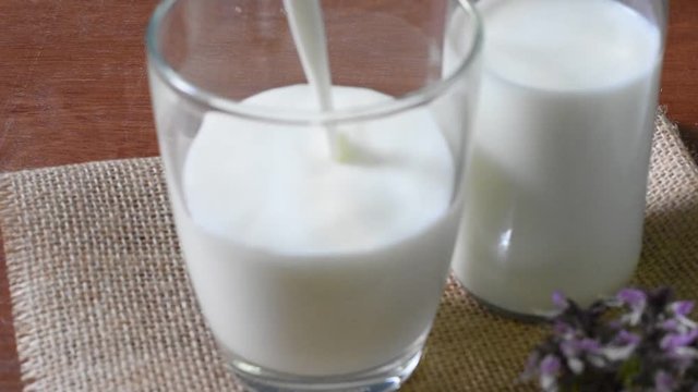 Pouring milk into a glass  and bottle of milk on wooden table with blue background,healthy drink,high calcium for kid elderly and pregnant women.