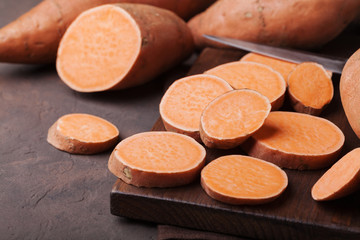 Organic raw sweet potato whole and sliced on wooden kitchen board.