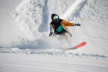 Young snowboarder in colorful sportswear riding with snowboard down powder snow hill