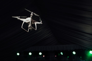 White quadrocopter fly inside the party-tent . Dark background, club light and soffits.