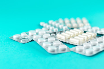 Packs of white capsules and pills packed in blisters with copy space on turquoise background. Focus on foreground, soft bokeh. Pharmacy drugstore concept