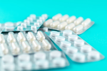 Packs of white capsules and pills packed in blisters with copy space on turquoise background. Focus on foreground, soft bokeh. Pharmacy drugstore concept