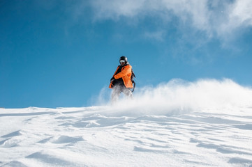 Fototapeta na wymiar Snowboarder in orange sportswear riding down the powder snow hill