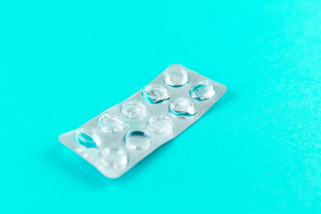 Empty pack of white pills packed in blister with copy space on turquoise background. Focus on foreground, soft bokeh. Pharmacy drugstore concept