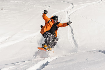 Young male snowboarder in orange sportswear jumping on the snow slope