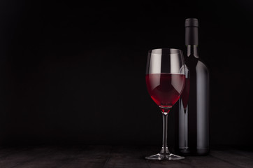Bottle of red wine and wine glass mock up on elegant dark black wooden background, copy space.