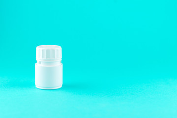 Close up white pill bottle on turquoise background with copy space. Focus on foreground, soft bokeh. Pharmacy drugstore concept