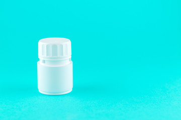 Close up white pill bottle on turquoise background with copy space. Focus on foreground, soft bokeh. Pharmacy drugstore concept