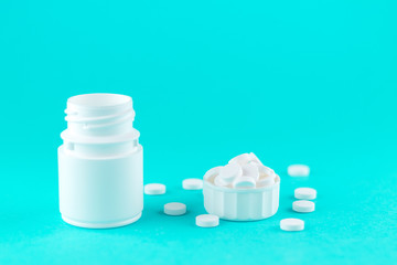 Close up white pill bottle with spilled out pills and capsules in cap on turquoise background with copy space. Focus on foreground, soft bokeh. Pharmacy drugstore concept