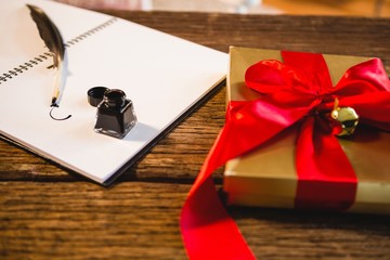 Wrapped gift, santa hat, diary and quill pen on wooden table in