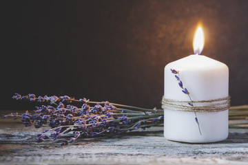 The burning white aroma candle against black wall with lavender bouquet on the wooden table. Copy space.