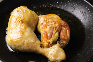 Two roasted chicken legs in black frying pan, close-up view