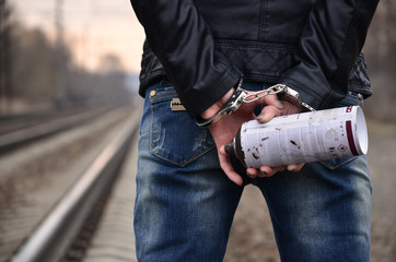 Girl in handcuffs with spraycan on the background of a railway track. The concept of vandalism prevention with the participation of the railway and trains.
