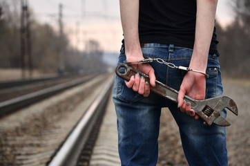 The girl in handcuffs with the adjustable wrench on the railway track background. The concept of crime prevention with the participation of the railway and trains.