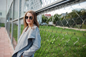 Girl in gray coat with sunglasses at small street stadium.