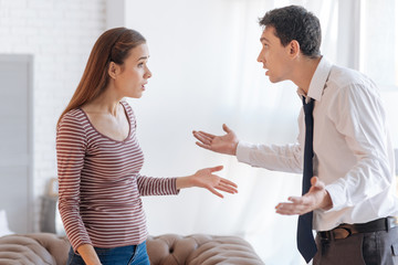 Accusations. Irritated emotional man looking at his angry nervous wife while sorting out the relationships with her