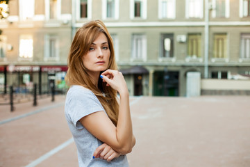 young thoughtfull redhead woman in a gray shirt walking around city. Concept of modern freedom hipster human