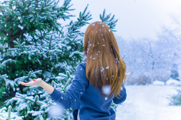 Happy cute woman in snow looking upwards. Winter weather theme image with a young woman smiling and hands up to catch snowflakes, by the lake shore, in village