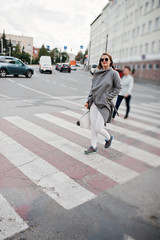 Girl in gray coat with sunglasses and handbag walking on the pedestrian crossing.