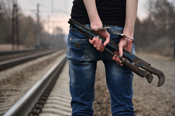 The girl in handcuffs with the pipe wrench on the railway track background. The concept of crime prevention with the participation of the railway and trains.
