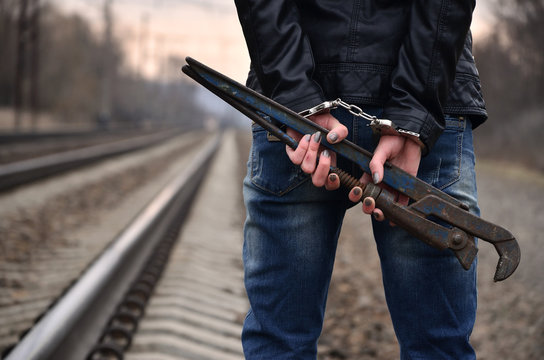 The girl in handcuffs with the pipe wrench on the railway track background. The concept of crime prevention with the participation of the railway and trains. - Powered by Adobe