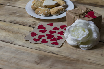 Small hearts on kraft paper. Biscuits, gift box with hearts and a white rose flower