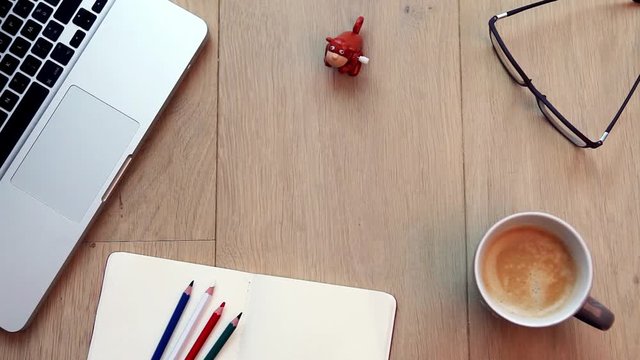 top view of a working desktop with a laptop, colored pencils, cup of coffee, glasses, and a monkey toy jumping in a continuous loop