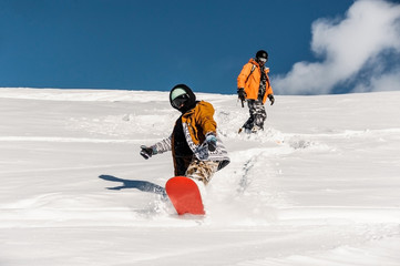 Two snowboarders in sportswear riding down the mountain slope