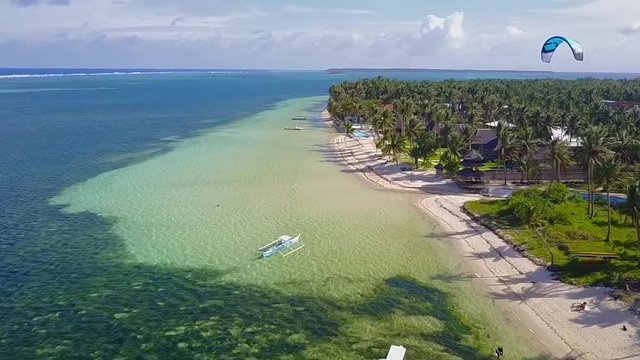 Aerial view of Kitesurfer cruising and jumping on empty blue water lagoon on tropical island