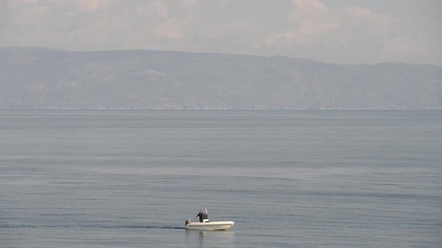 Pescatore sulla sua barca mentre pesca sul mare calmo e pieno ri riflessi