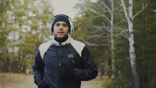 Tracking shot of Handsome runner man in headphones jogging while listening music in winter park in the morning