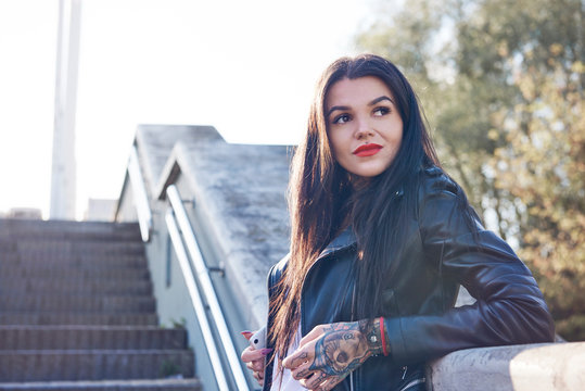 Portrait of young woman leaning against wall, pensive expression, tattoos on hand
